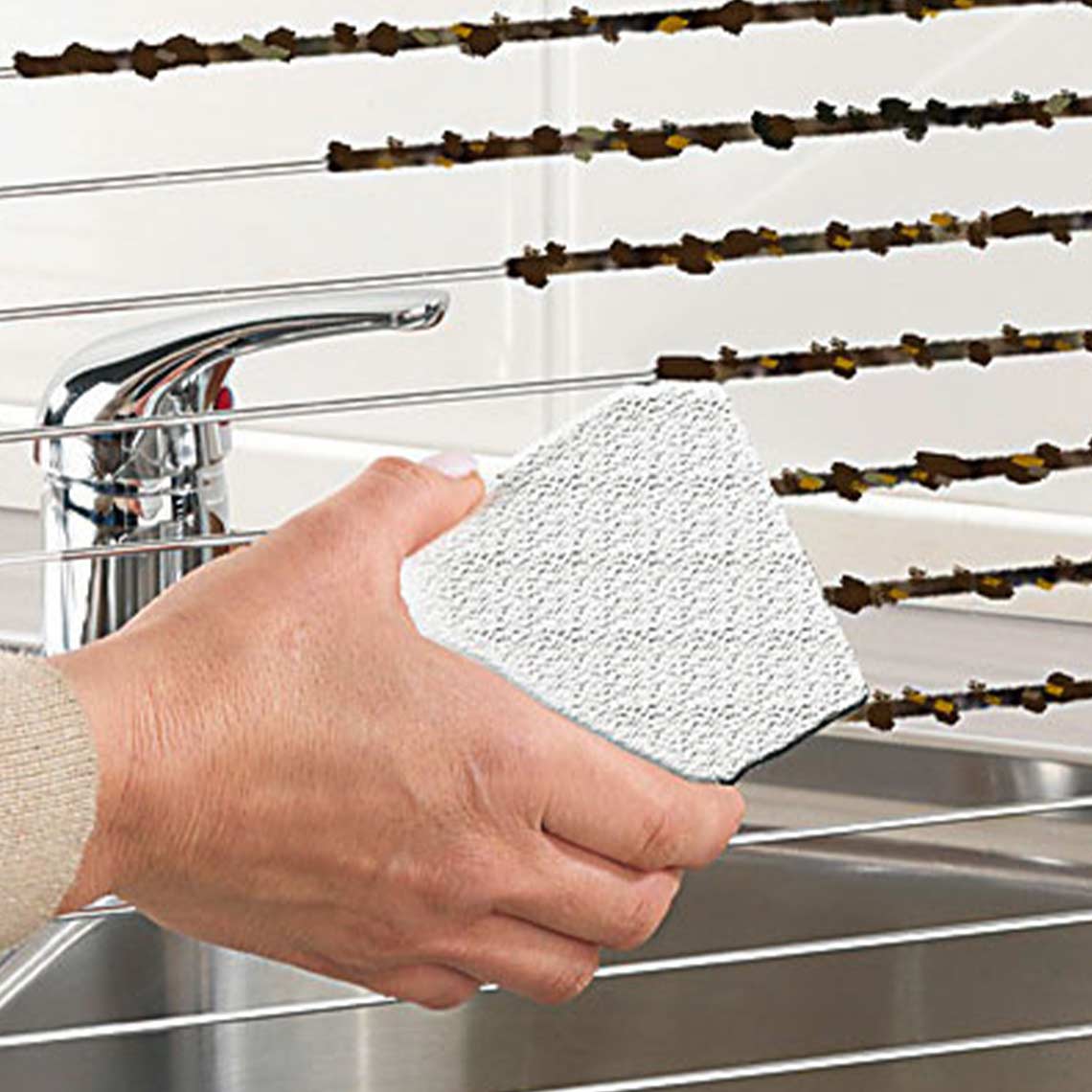 Detail van een hand die met het reinigingsblok een aangekoekt grillrooster boven een gootsteen schoonmaakt 2