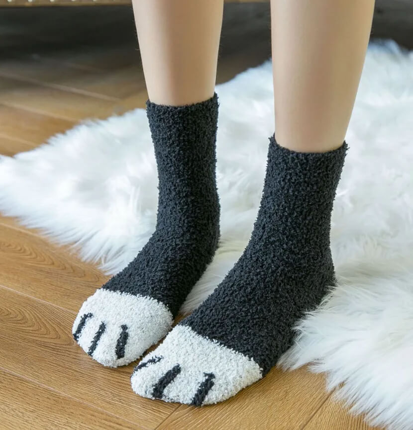 Gedragen zwarte pluchen sokken met witte voorvoet en zwarte geborduurde tenen, op een wit vachtkleed