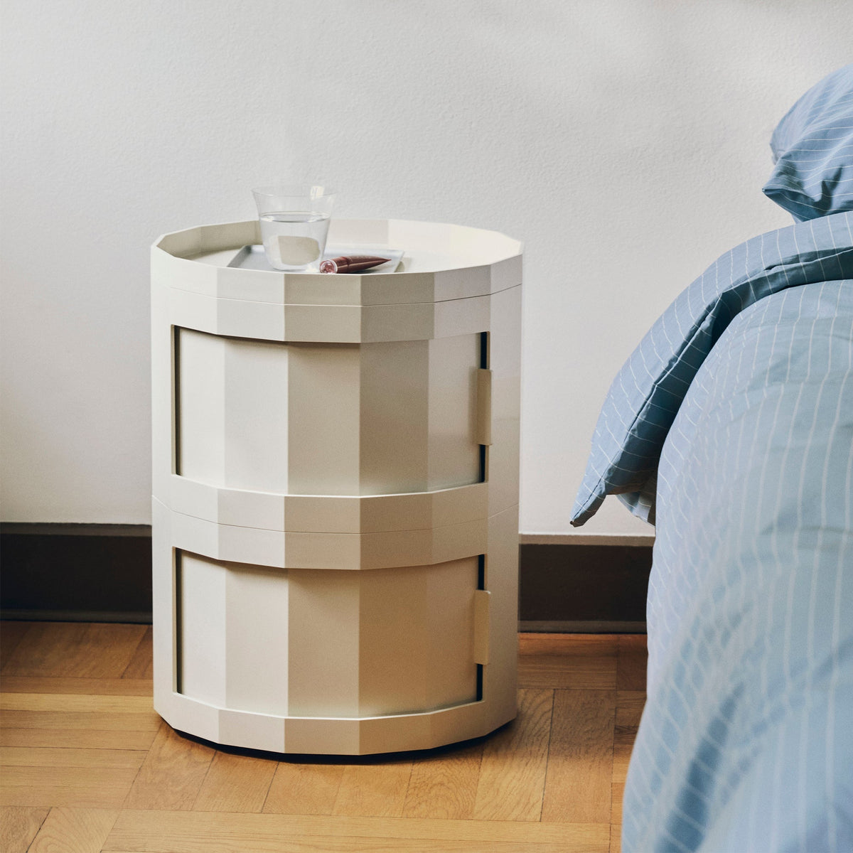 Crèmekleurige tweedelige ronde kast als nachtkastje naast een bed met een glas water erop 52