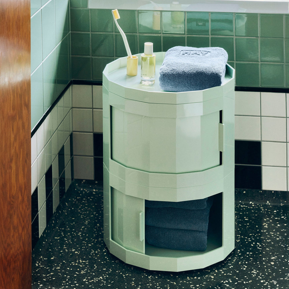 Mintgroene ronde kast in een betegelde badkamer, onderste deur open met handdoeken, toiletspullen op het blad 35