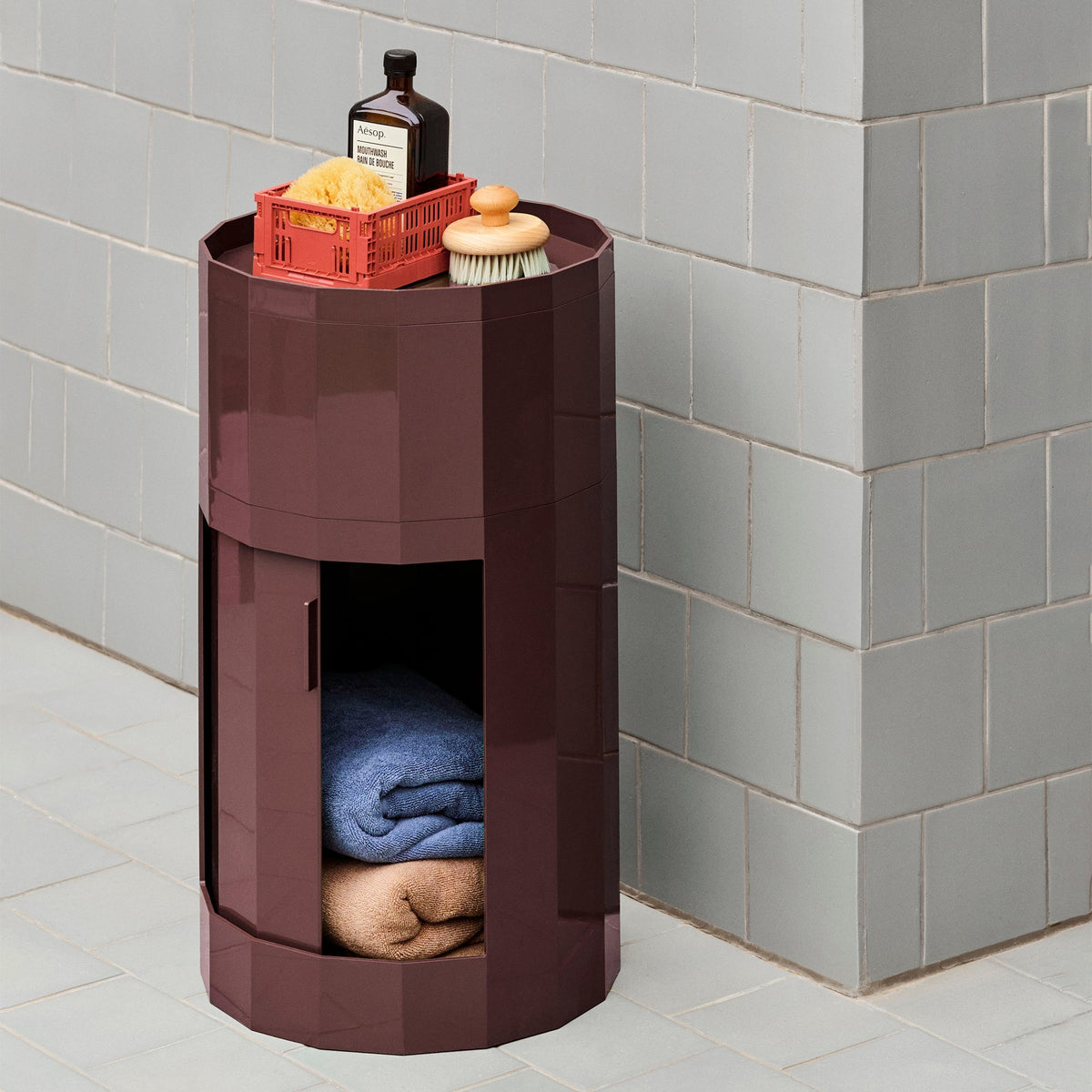 Bordeauxrode ronde kast in een badkamer met geopende deur, handdoeken en toiletartikelen bovenop 47