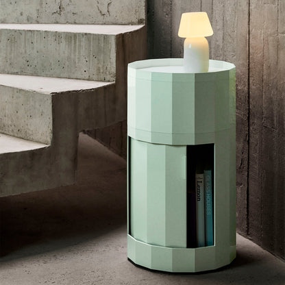 Lichtgroene kast met open deur met boeken en brandende lamp bovenop naast betonnen trap
