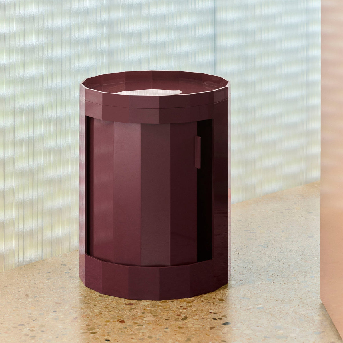 Bordeauxrode ronde kast met gesloten deur op een terrazzo plank voor geribbeld glas 49