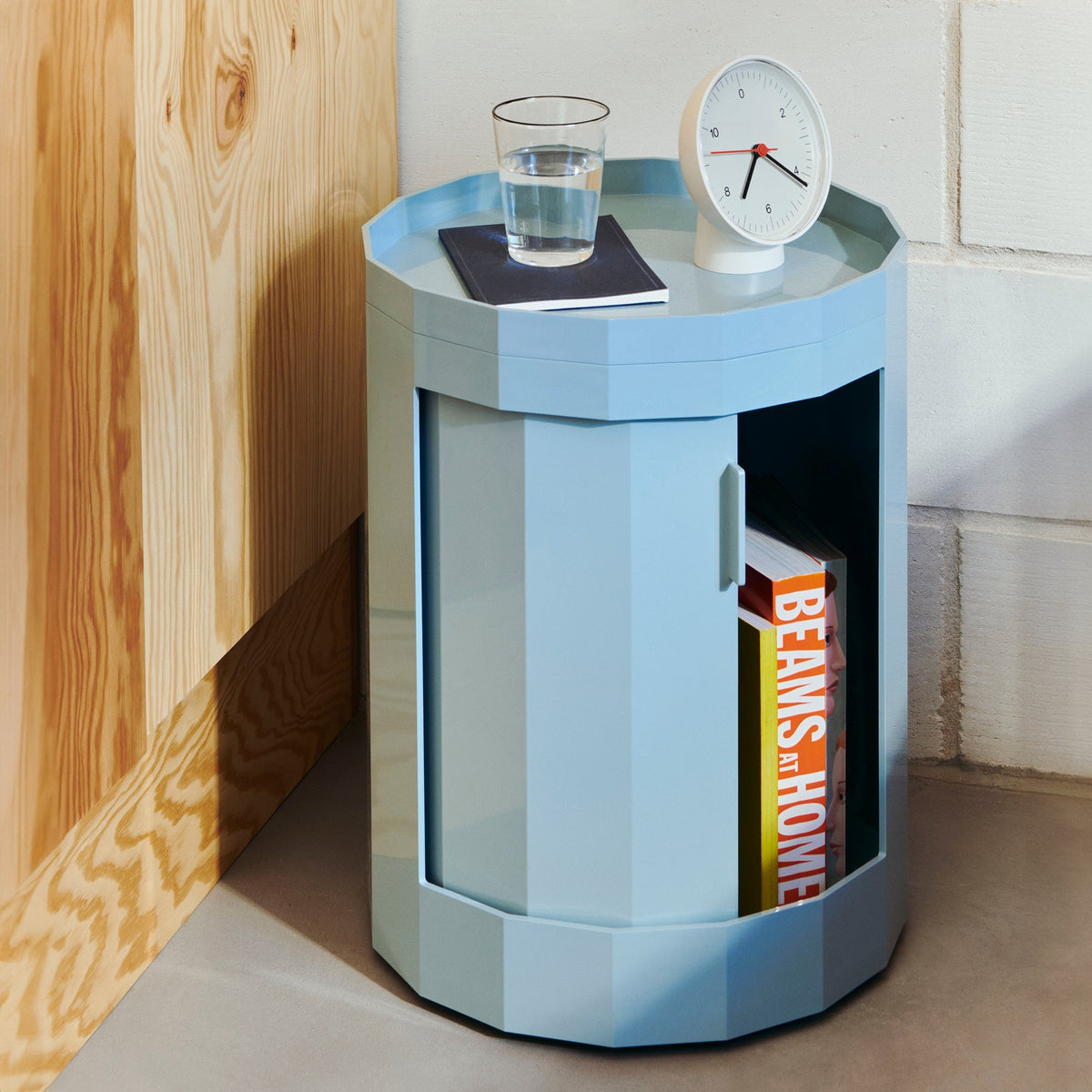 Lichtblauwe lage kast met open deur met boeken en glas water en wekker bovenop