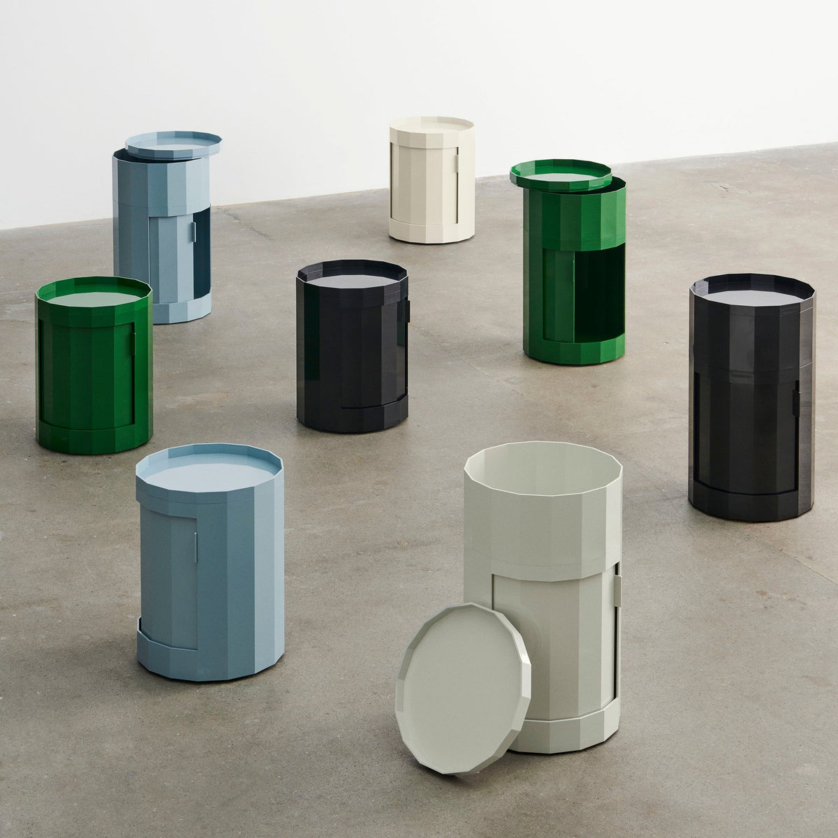 Groep ronde kasten in blauw, groen, zwart en crème op een betonnen vloer, sommige met afgenomen deksel 46