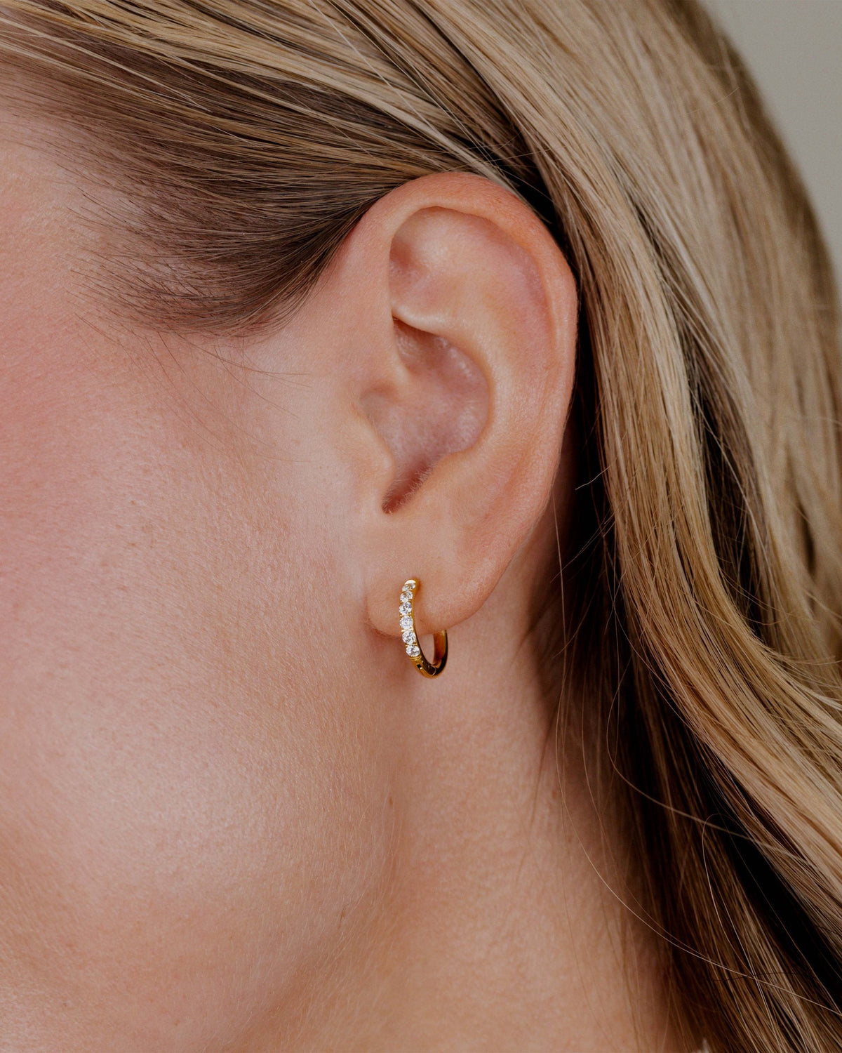 Gouden oorring met kleine zirkonia in het oor van een blonde vrouw