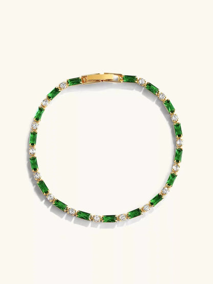 Detail van de losse gouden armband met afwisselend groene rechthoekige en ronde heldere stenen, gesp bovenaan op een lichte