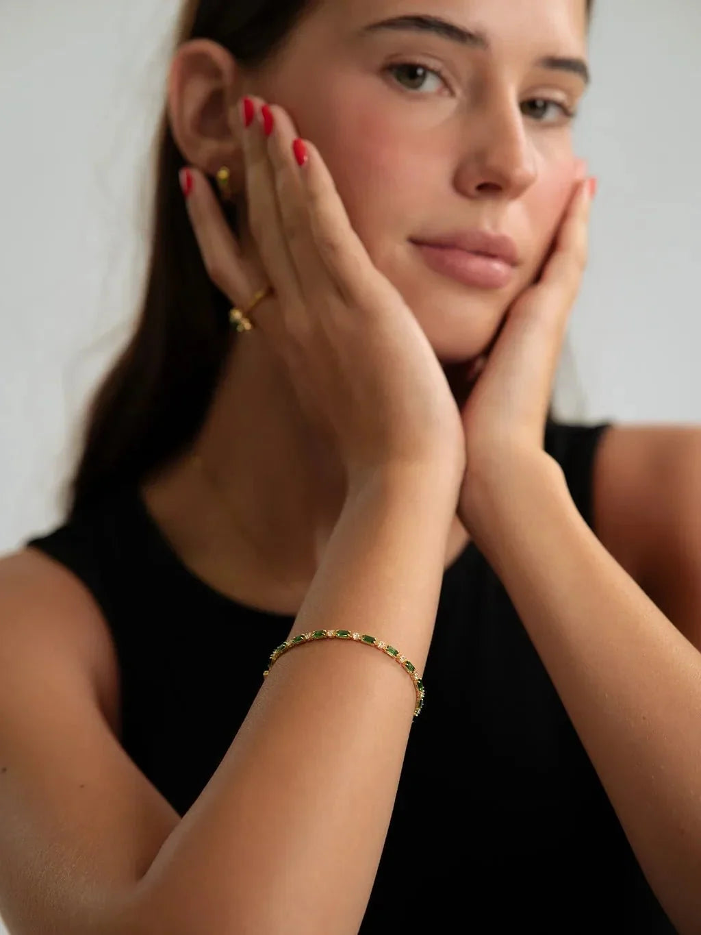Model met rode nagels en handen tegen haar gezicht draagt de groene armband om de pols