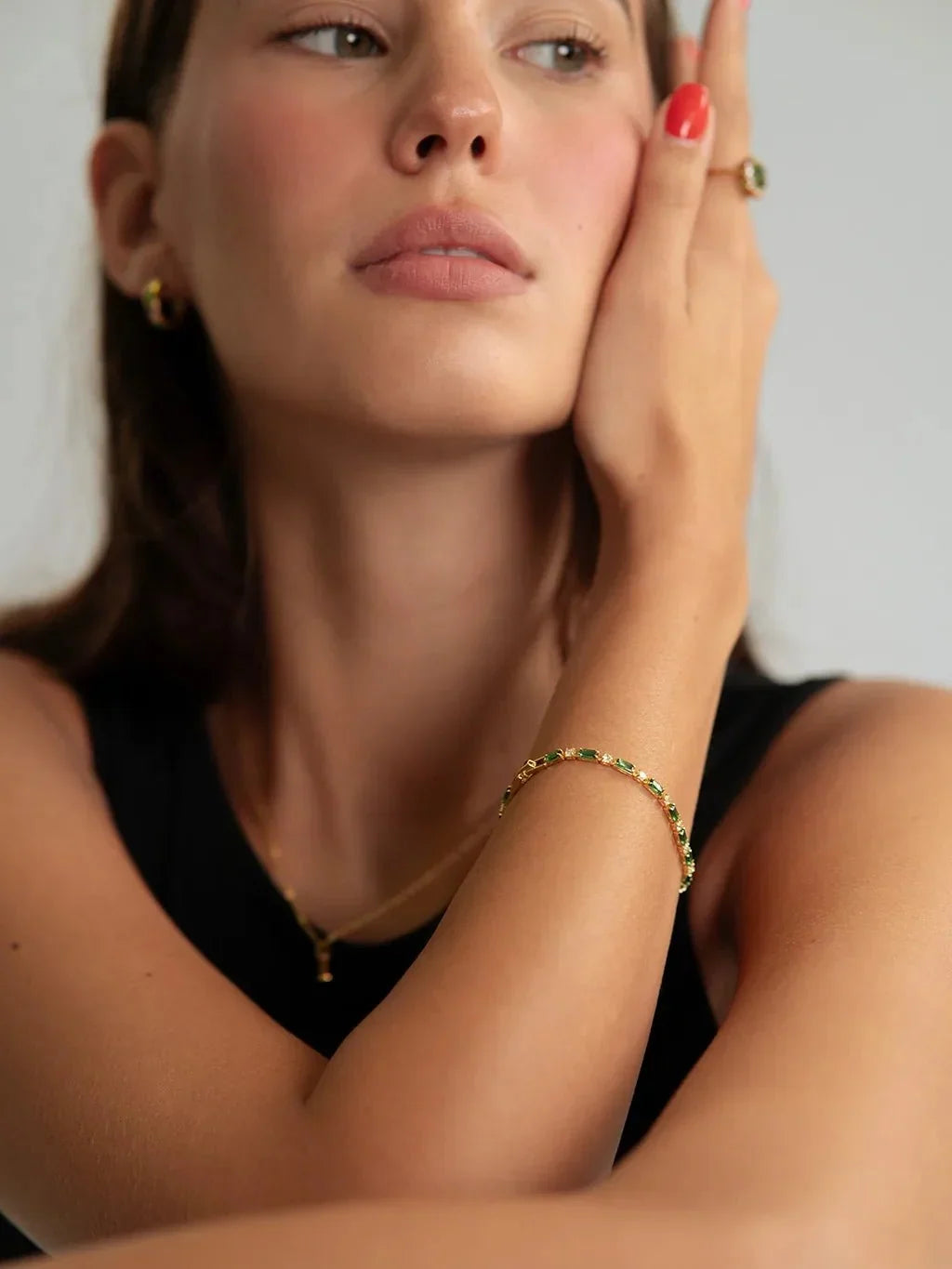 Model in zwart topje leunt met haar hand tegen haar wang en draagt de groene armband