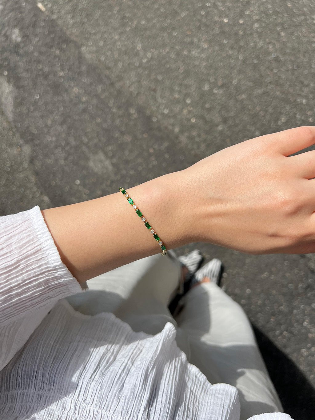 Detail van de pols met de armband van groene en heldere stenen, gedragen bij een witte blouse buiten