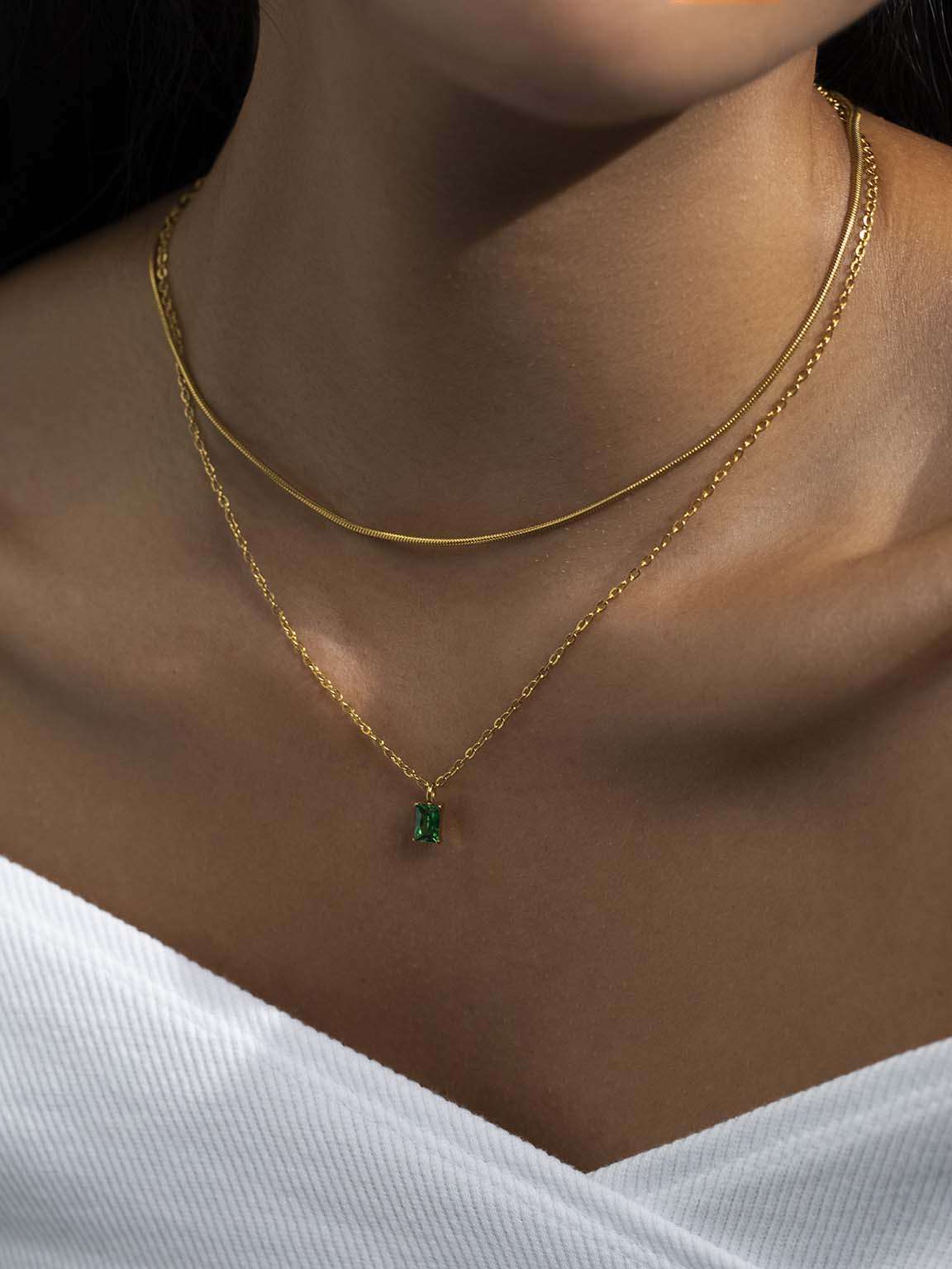 Detail van de ketting met groene hanger gedragen samen met een dunne gouden slangenketting op een wit topje