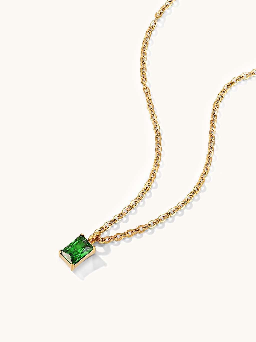 Detail van de gouden ketting met groene rechthoekige hanger op een lichte achtergrond