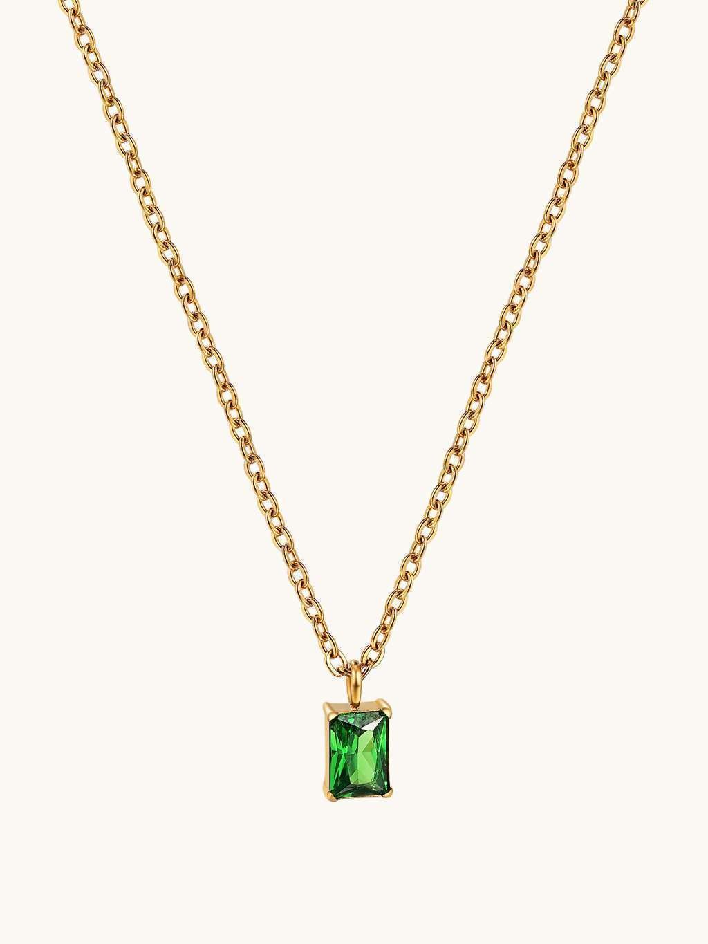 Detail van de voorkant van de gouden schakelketting met groene rechthoekige steen als hanger op een lichte achtergrond