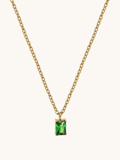 Detail van de voorkant van de gouden schakelketting met groene rechthoekige steen als hanger op een lichte achtergrond