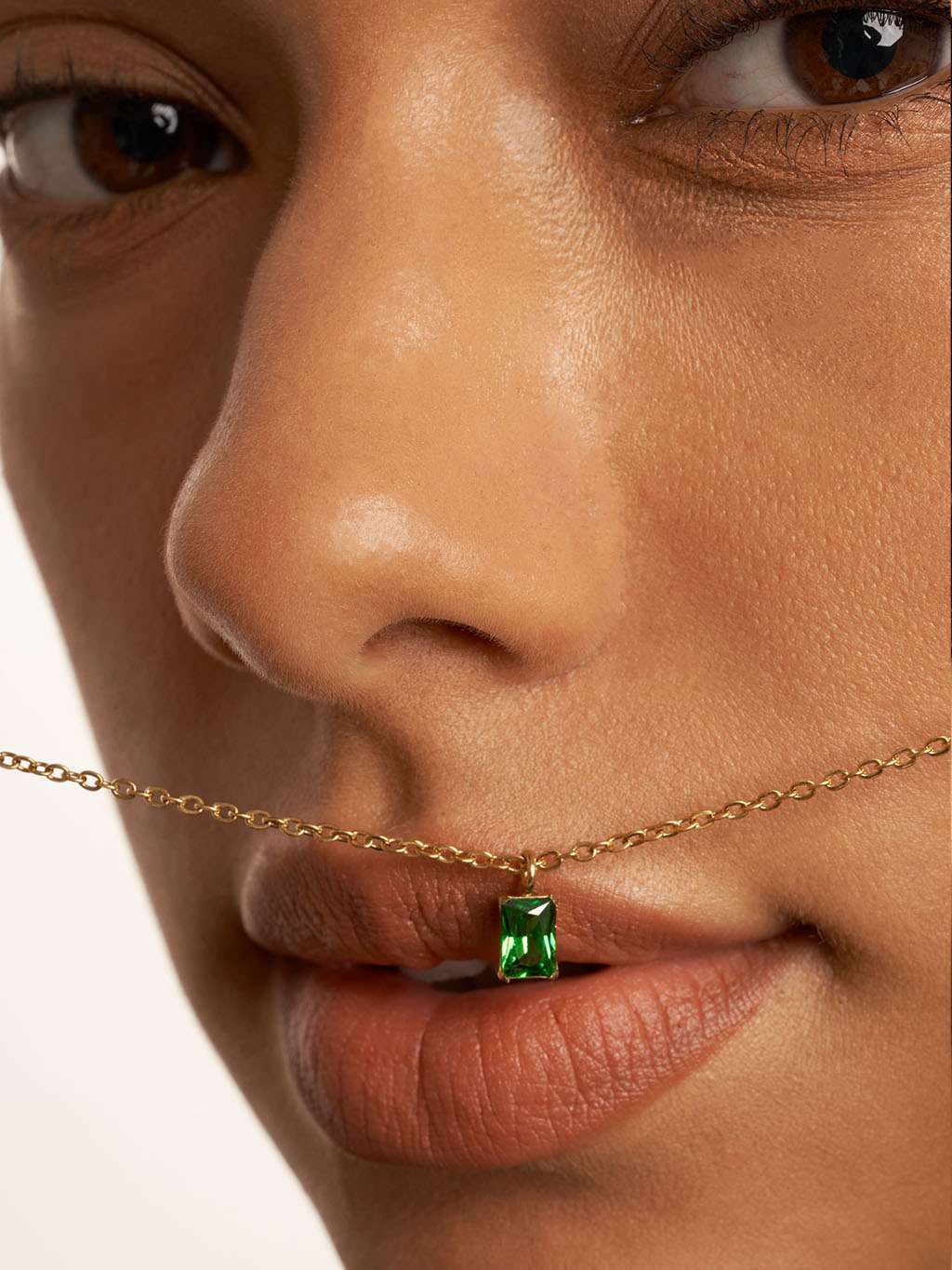 Detail van het gezicht van een model met de ketting vlak voor de lippen, hanger zichtbaar
